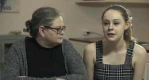 Mæðgur sitja hlið við hlið. Móðirinn lítur á unglingsdóttur sína