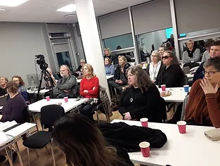 Fjöldi fólks situr við borð að fylgjast með fyrirlesara