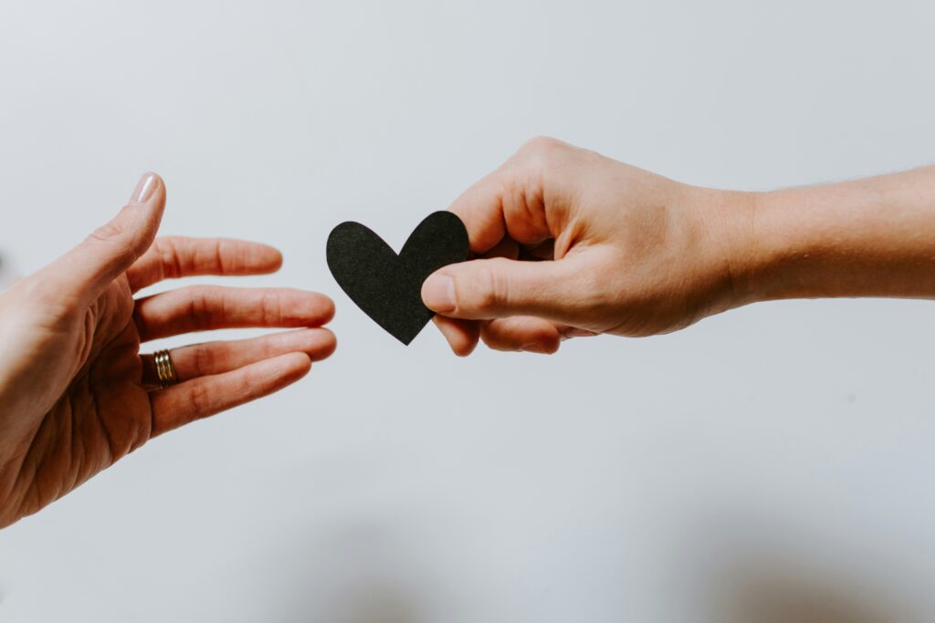 kelly-sikkema-XX2WTbLr3r8-unsplash Útrétt hönd afhendir útklippt pappírshjarta og önnur hönd tekur á móti
