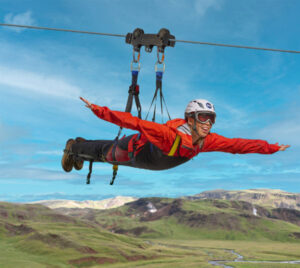 Manneskja í rauðum galla og hjálm hangir úr Zipline í „flugvéla“ stellingu